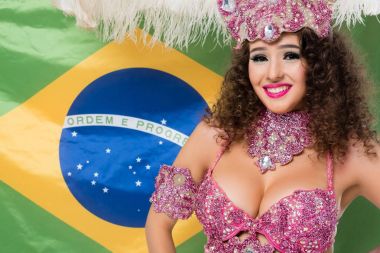 Cheerful woman in carnival costume with pink feathers on Brasil flag background clipart