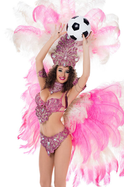 cheerful woman in carnival costume with pink feathers holding soccer ball, isolated on white