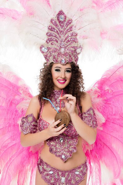 woman in carnival costume holding coconut with straws and looking at camera, isolated on white    