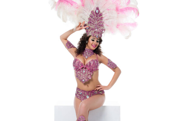 Bright woman in carnival costume with pink feathers sitting and posing seductively isolated on white