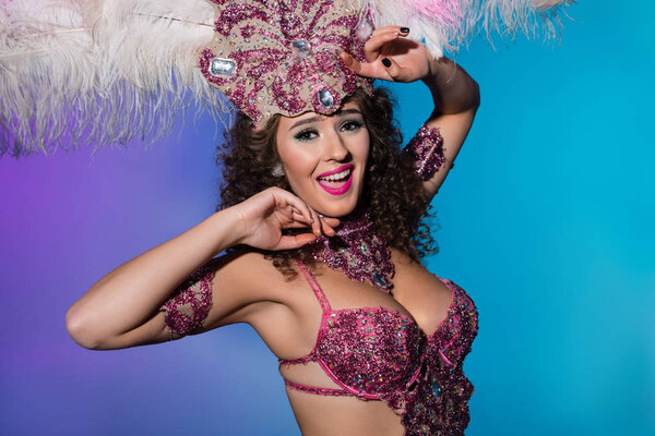 Cheerful woman in carnival costume with pink feathers isolated on blue background