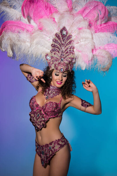 Happy young woman in carnival costume with pink feathers on blue background