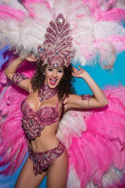 Happy young woman in carnival costume with pink feathers performing isolated on blue background clipart