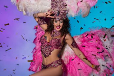 Cheerful woman in carnival costume with pink feathers dancing emotionally isolated on blue background clipart