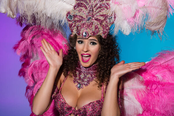 Cheerful woman in carnival costume with pink feathers laughing isolated on blue background