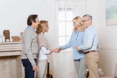 Couple of middle aged man and woman greeting their friends as guests and shaking hands clipart