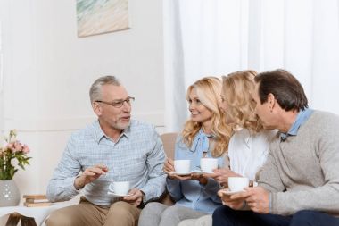 Senior men and women enjoying time together while drinking tea on sofa clipart