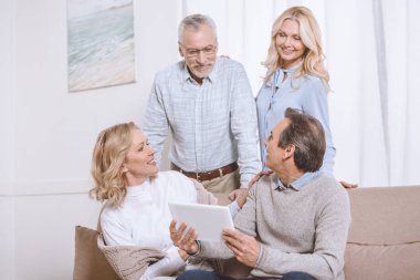 Senior men and women using digital tablet while sitting on sofa clipart