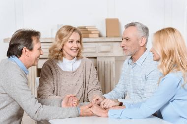 friends sitting at table and holding hands of each other while praying  clipart