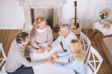 friends sitting at table and holding hands of each other while praying clipart