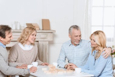 happy friends sitting at table with tea and playing tower game    clipart