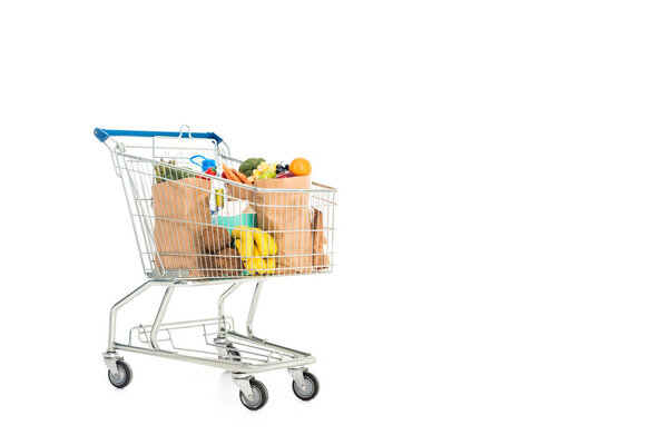 paper bags full of fruits and vegetables in shopping trolley isolated on white