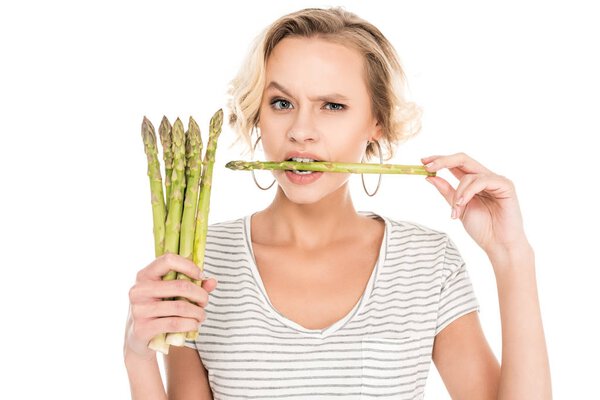 portrait of young woman biting raw asparagus in hands isolated on white