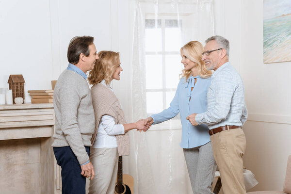 Couple of middle aged man and woman greeting their friends as guests and shaking hands