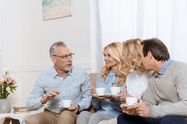 Senior men and women enjoying time together while drinking tea on sofa