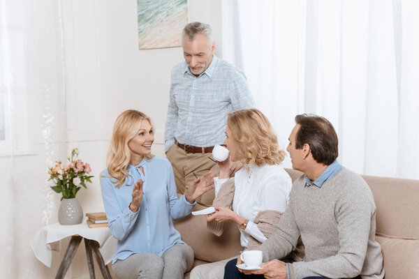Senior men and women having a conversation while drinking tea on sofa