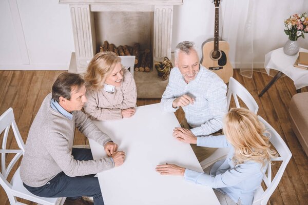 overhead view of friends sitting at table and speaking at room interior 