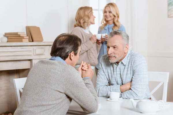 men speaking at table while women standing on background 