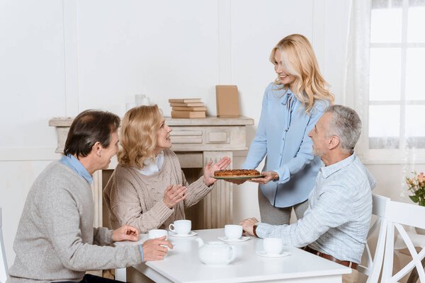 woman serving pie on table for sitting friends members 
