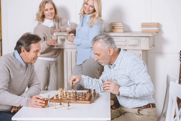 Mannen Spelen Schaak Zittend Aan Tafel Staande Vrouw Met Bril — Gratis stockfoto