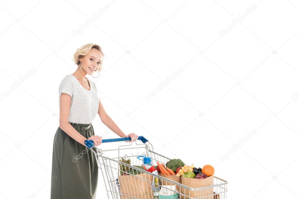 attractive young woman standing with shopping trolley and smiling at camera isolated on white 