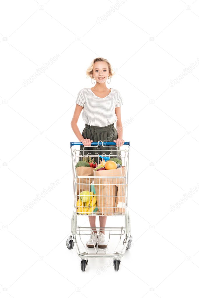 beautiful young woman standing with shopping trolley and smiling at camera isolated on white  