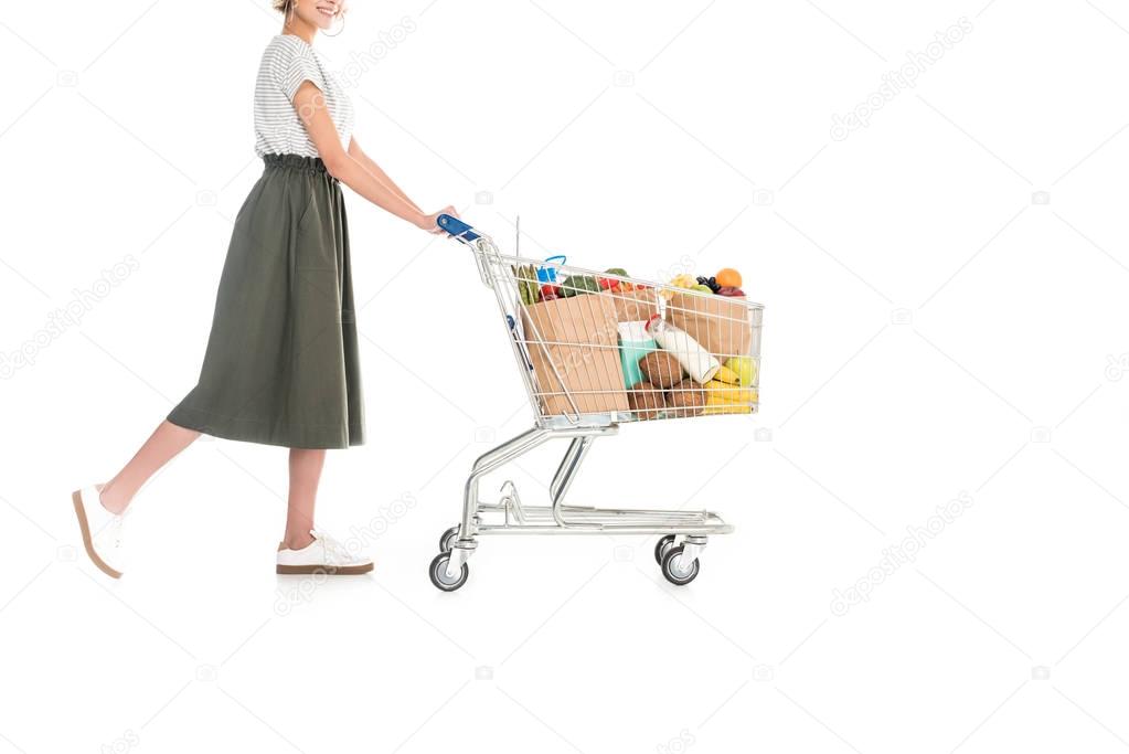 partial side view of woman pushing shopping trolley with grocery bags isolated on white