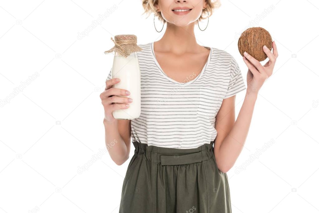 partial view of smiling woman holding coconut and coconut milk in hands isolated on white