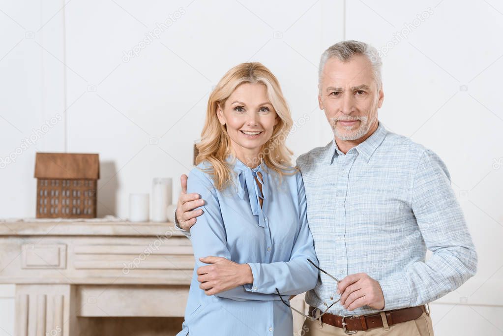 Mature man and woman hugging by fireplace in cozy room