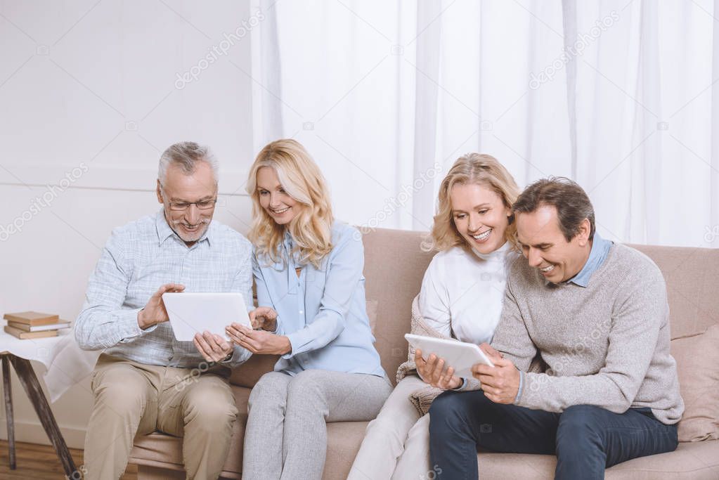 Senior men and women using digital tablets while sitting on sofa