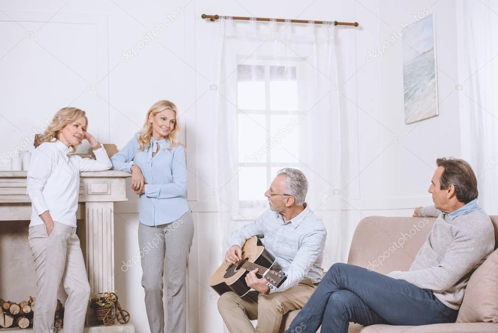 Middle aged men and women listening to guitar music in living room