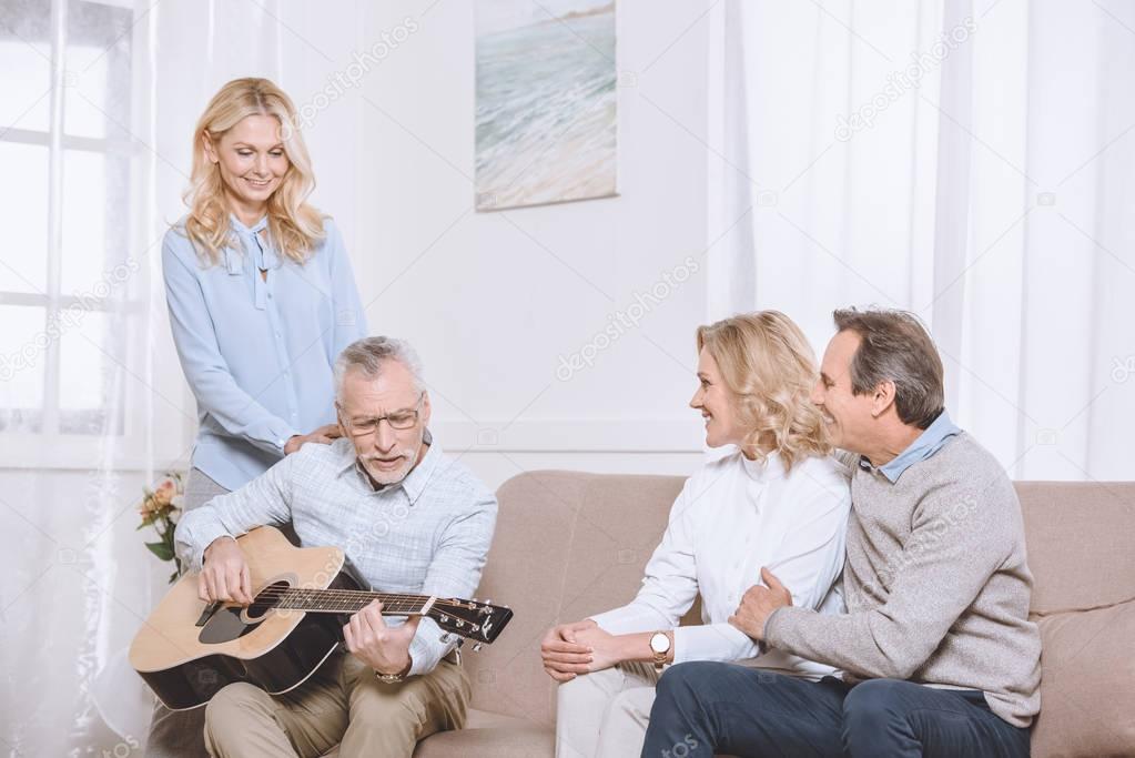 Middle aged men and women listening to guitar music in living room