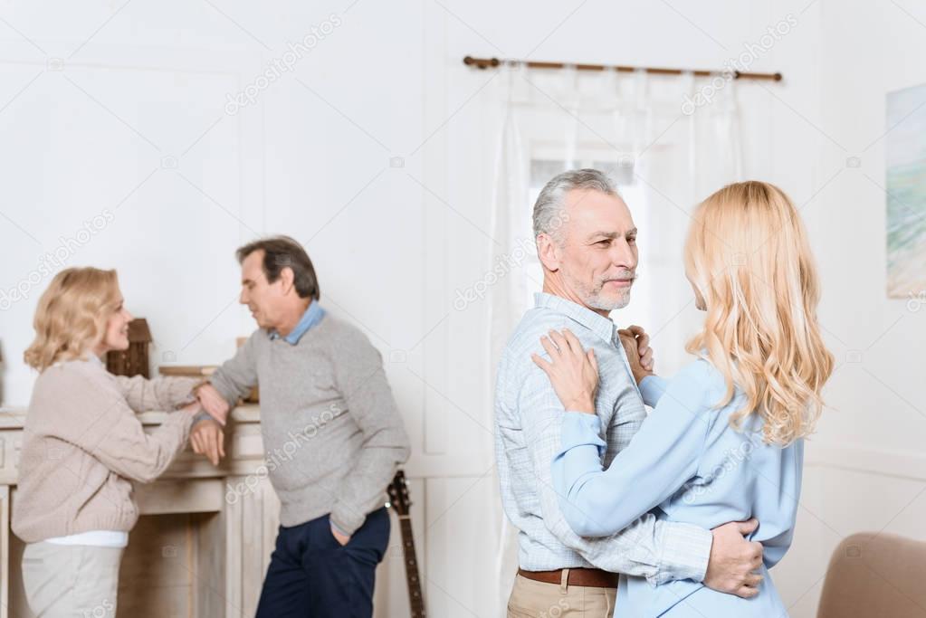 Middle aged men and women dancing by fireplace in cozy room