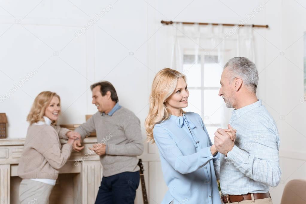 Middle aged men and women dancing and talking by fireplace in cozy room