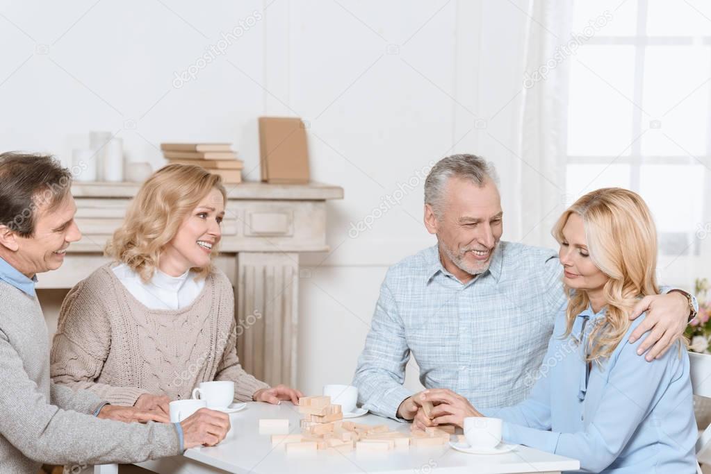 happy friends sitting at table with tea and playing tower game   