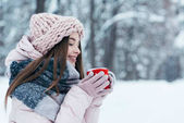 side view of beautiful young woman with cup of hot coffee in hands in snowy park