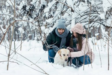 young couple having fun together with dog in winter park clipart