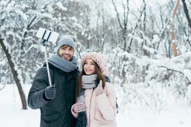 smiling couple taking selfie together on smartphone in winter park clipart