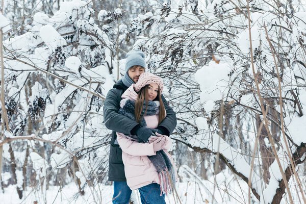 Молодой человек обнимает девушку в зимнем лесу
