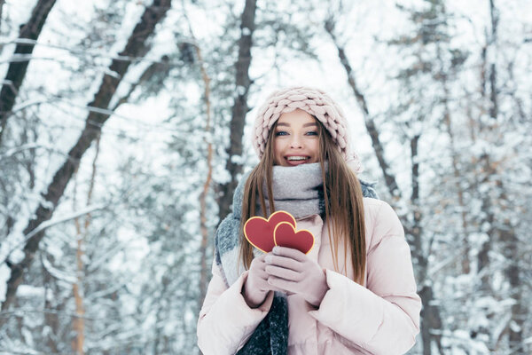 portrait of beautiful young woman with hearts in hands looking at camera in snowy park