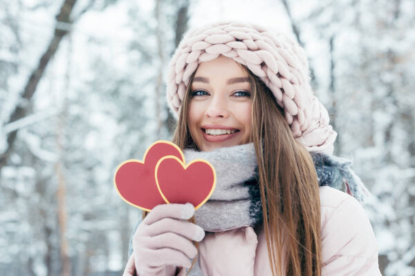 portrait of beautiful young woman with hearts in hand looking at camera in snowy park