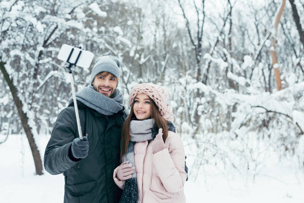 улыбающаяся пара делает селфи вместе на смартфоне в зимнем парке
