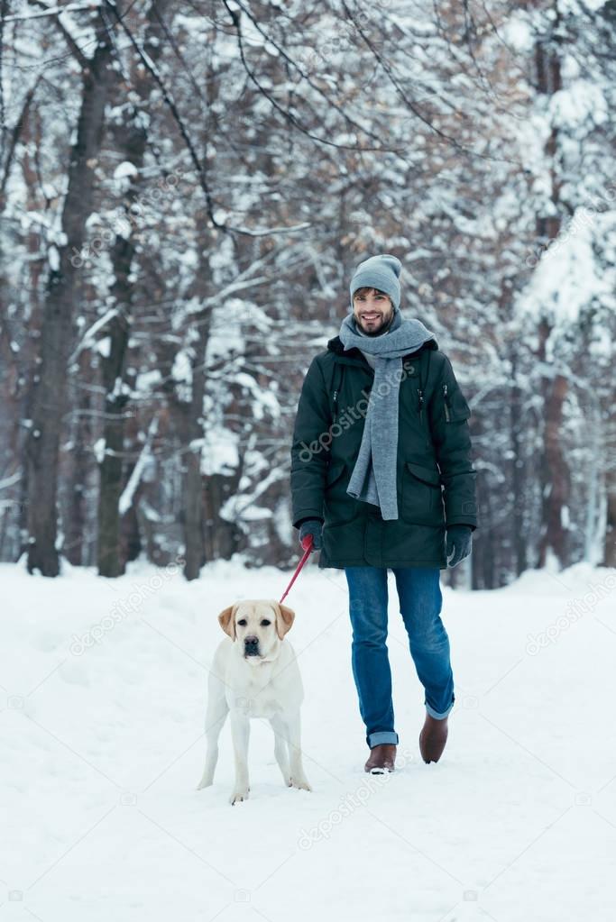 young man walking with dog on leash in winter park