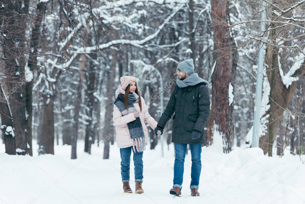 young smiling couple holding hands and walking in winter park