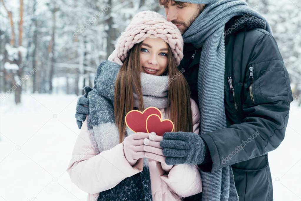 tender couple with red hearts in snowy park on winter day