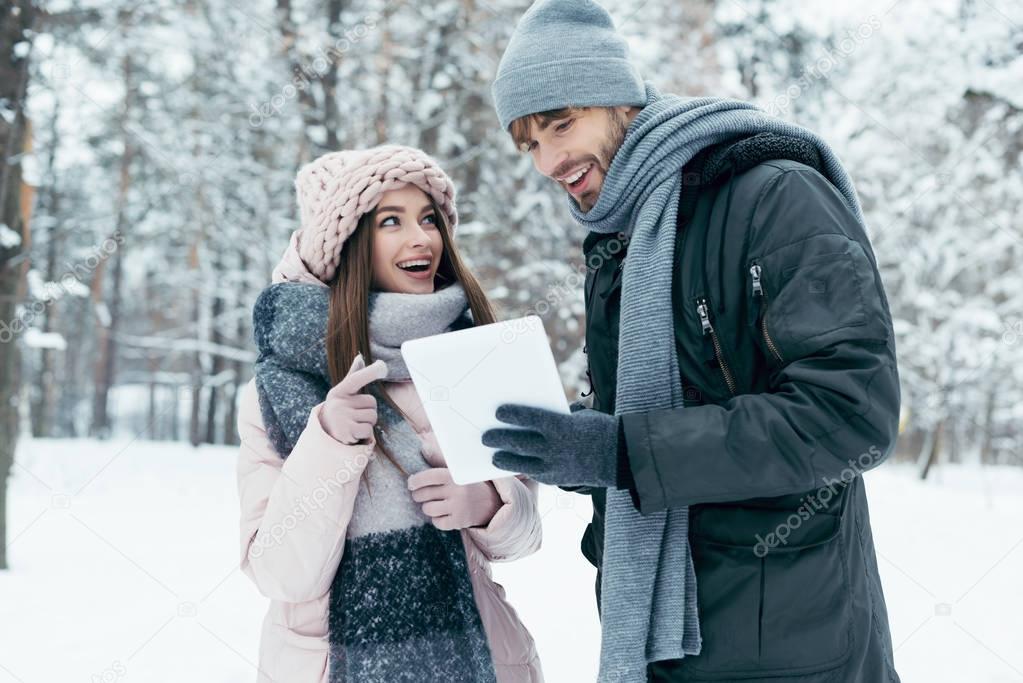 portrait of young happy couple with tablet in snowy park