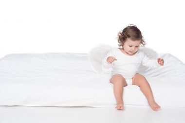 adorable happy baby with wings sitting on bed, isolated on white clipart