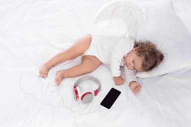 küçük melek kanatlı kulaklık ve smartphone ile yatakta yatarken