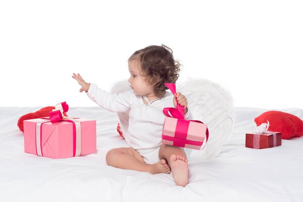 cute baby angel sitting on bed with presents, isolated on white