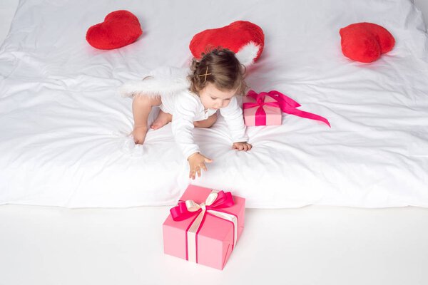 little cherub with wings on bed with hearts and presents